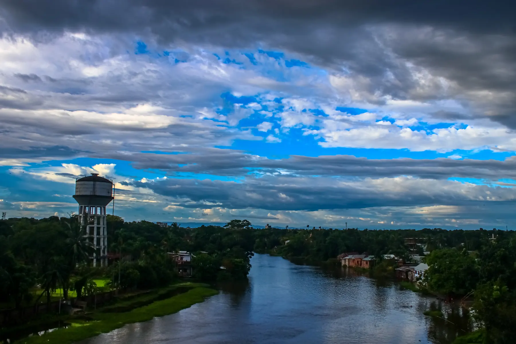 A river landscape with a water tower under a blue sky