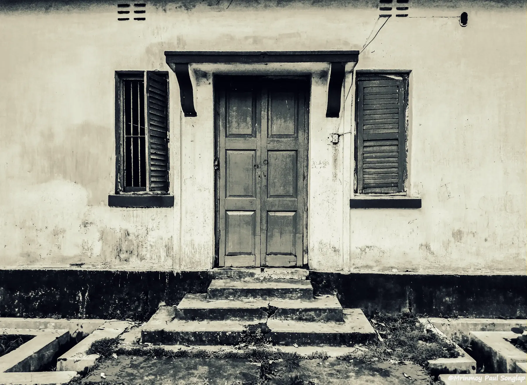 A weathered building facade with a door and shuttered windows